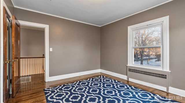 empty room featuring baseboards, radiator, crown molding, and wood finished floors