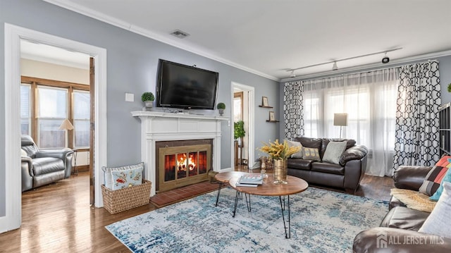 living room with wood finished floors, a healthy amount of sunlight, visible vents, crown molding, and a glass covered fireplace