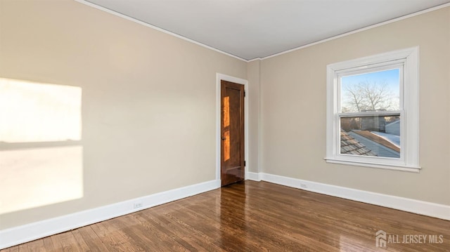 empty room with crown molding, wood finished floors, and baseboards