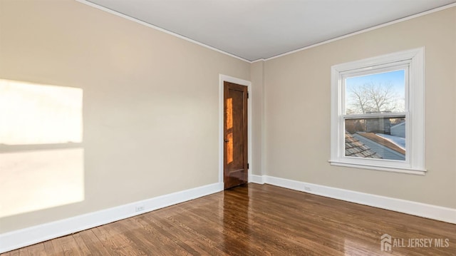 empty room with baseboards, crown molding, and wood finished floors