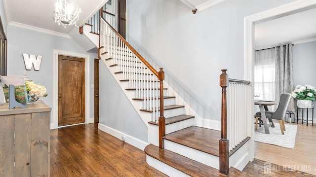 stairs with ornamental molding, a notable chandelier, baseboards, and wood finished floors