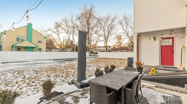 snow covered patio with central AC, outdoor dining space, and fence