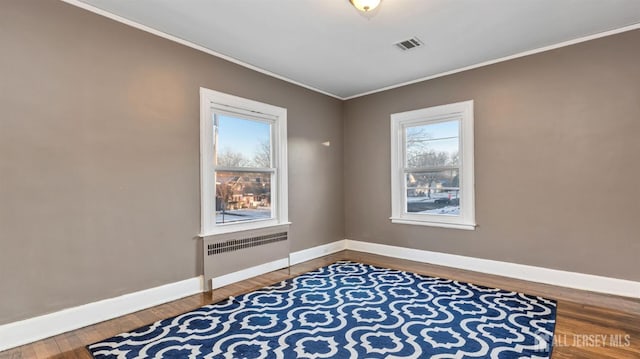 unfurnished room featuring baseboards, radiator heating unit, visible vents, crown molding, and wood finished floors