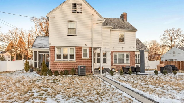 snow covered rear of property with a sunroom, entry steps, a chimney, and fence