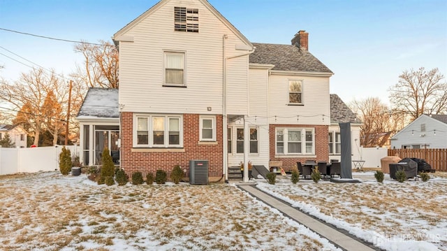 snow covered property with a chimney, brick siding, a patio, a sunroom, and a fenced backyard