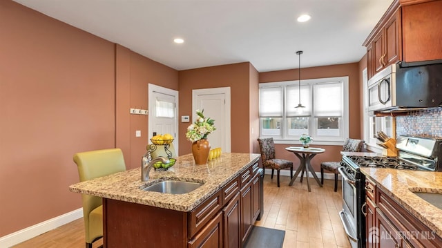 kitchen featuring baseboards, light wood finished floors, a sink, a kitchen island, and appliances with stainless steel finishes