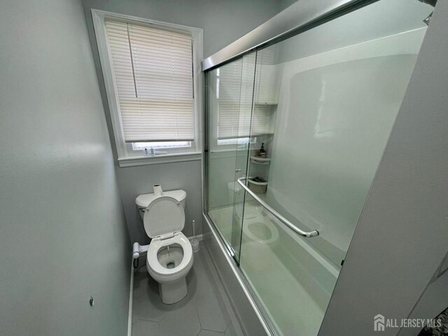 bathroom with toilet, bath / shower combo with glass door, and tile patterned flooring