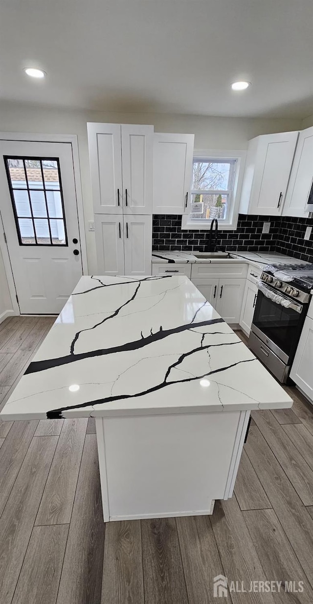 kitchen with a kitchen island, gas range, light stone countertops, and sink