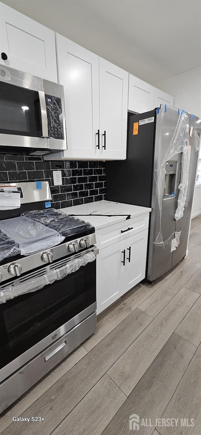 kitchen with tasteful backsplash, white cabinetry, appliances with stainless steel finishes, and light hardwood / wood-style flooring