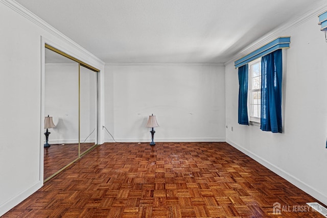 empty room with visible vents, crown molding, and baseboards