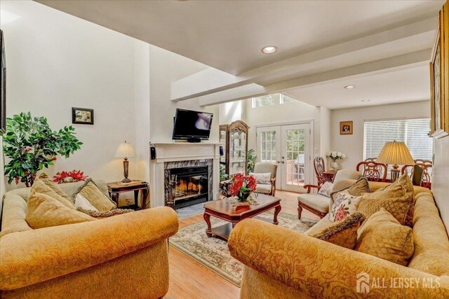 living room with beam ceiling, a fireplace, light hardwood / wood-style flooring, and french doors