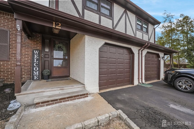 doorway to property with aphalt driveway, brick siding, an attached garage, and stucco siding