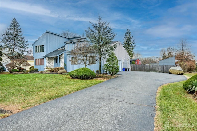 view of front of home with fence, a front yard, a garage, stone siding, and driveway