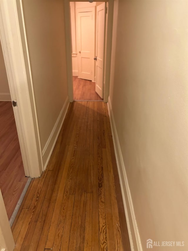 hall featuring dark wood-style flooring and baseboards