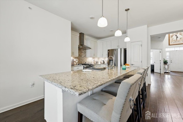 kitchen with dark wood finished floors, a kitchen breakfast bar, tasteful backsplash, wall chimney range hood, and appliances with stainless steel finishes