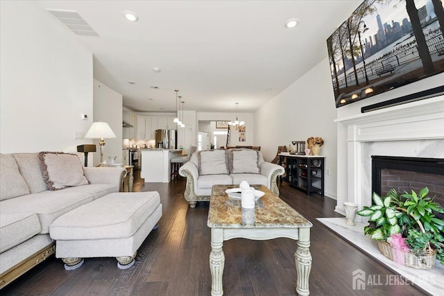 living area with recessed lighting, dark wood finished floors, visible vents, a fireplace, and a notable chandelier