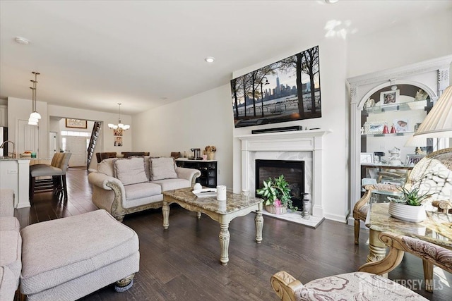 living room featuring recessed lighting, dark wood-type flooring, a notable chandelier, and a premium fireplace