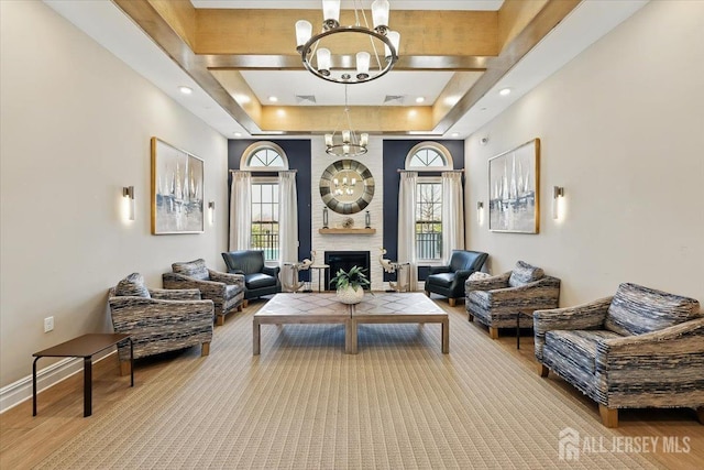 sitting room featuring a large fireplace, baseboards, an inviting chandelier, a tray ceiling, and wood finished floors