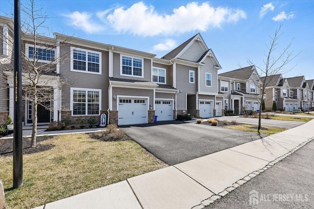 townhome / multi-family property featuring a garage, a residential view, driveway, and stone siding
