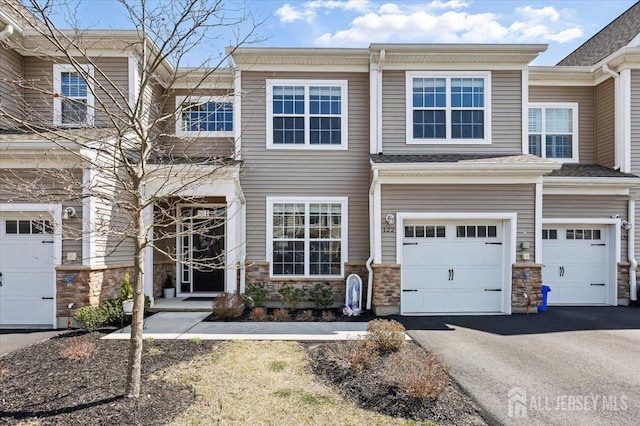 townhome / multi-family property with driveway, stone siding, and a garage