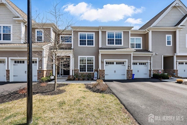 townhome / multi-family property with stone siding, driveway, a front yard, and a garage