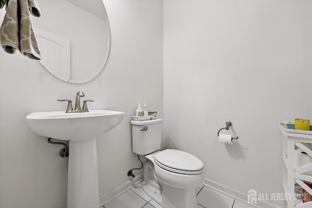 half bath with tile patterned flooring, toilet, baseboards, and a sink
