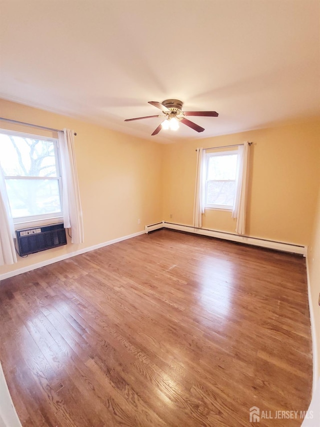 empty room with a wall mounted AC, a baseboard heating unit, wood finished floors, baseboards, and ceiling fan