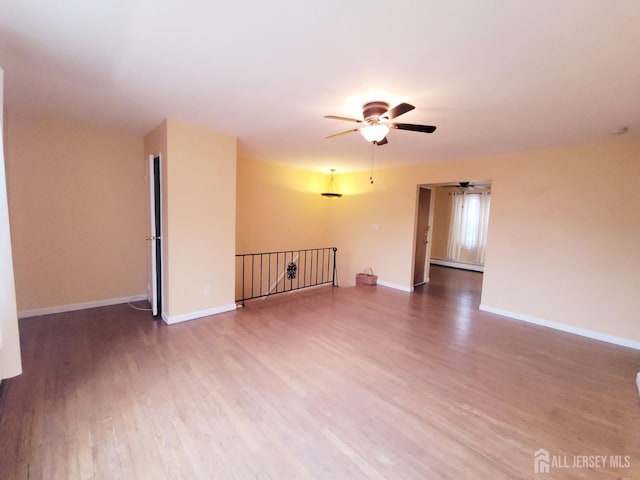 unfurnished room with ceiling fan, a baseboard heating unit, baseboards, and wood finished floors