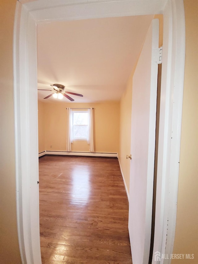 empty room featuring a baseboard heating unit, a ceiling fan, and wood finished floors