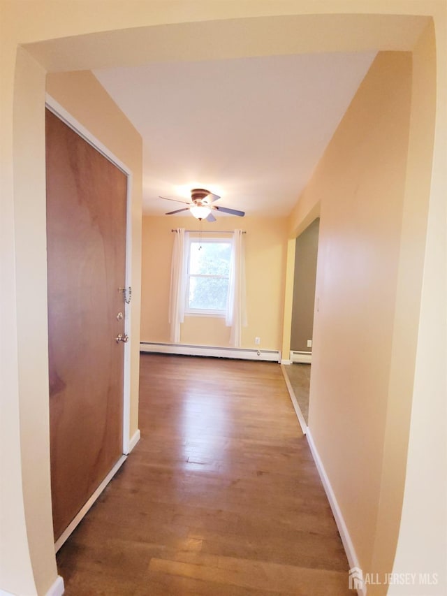 corridor with a baseboard heating unit, baseboards, and wood finished floors