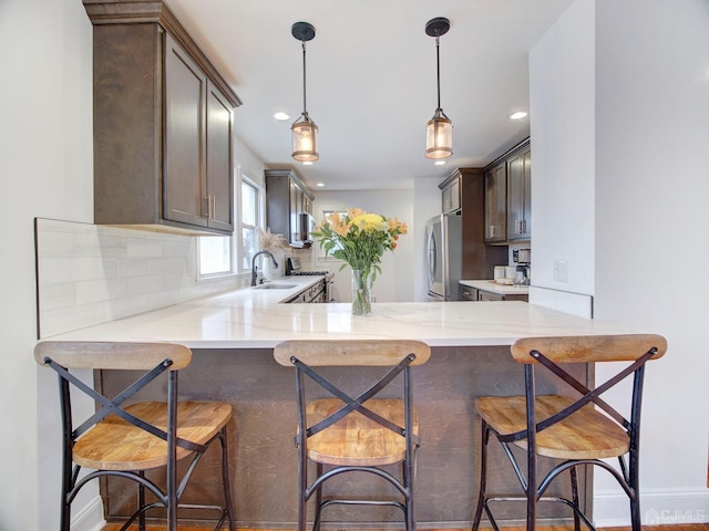 kitchen with sink, stainless steel fridge, a breakfast bar, backsplash, and dark brown cabinetry