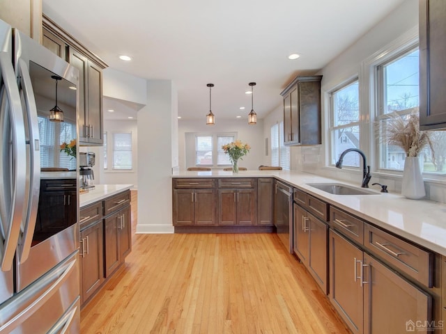 kitchen with pendant lighting, sink, stainless steel appliances, decorative backsplash, and light wood-type flooring