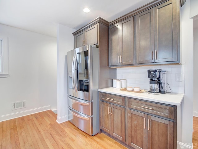 kitchen with dark brown cabinets, light hardwood / wood-style floors, stainless steel fridge with ice dispenser, and decorative backsplash