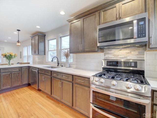 kitchen featuring pendant lighting, sink, backsplash, stainless steel appliances, and light hardwood / wood-style flooring