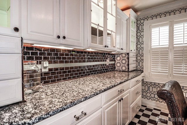 kitchen with dark stone counters, decorative backsplash, white cabinets, glass insert cabinets, and dark floors