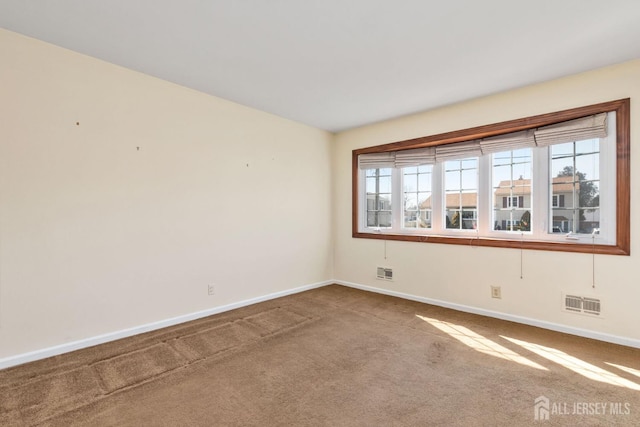 empty room with carpet floors, visible vents, and baseboards