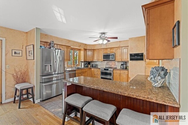 kitchen with kitchen peninsula, light stone counters, a breakfast bar, and stainless steel appliances