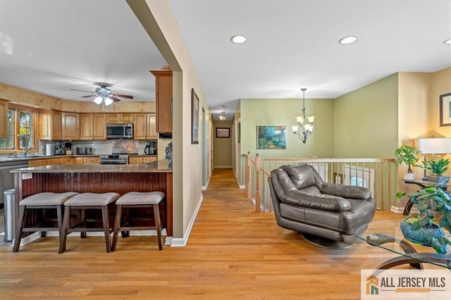 kitchen with stainless steel appliances, light hardwood / wood-style flooring, backsplash, kitchen peninsula, and decorative light fixtures