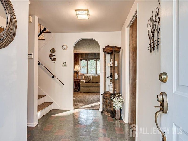 foyer featuring stairs, baseboards, arched walkways, and stone finish flooring