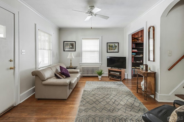 living area with stairs, radiator heating unit, ornamental molding, wood finished floors, and arched walkways