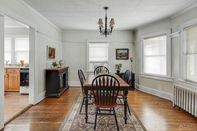 dining space featuring radiator, baseboards, ornamental molding, an inviting chandelier, and wood-type flooring