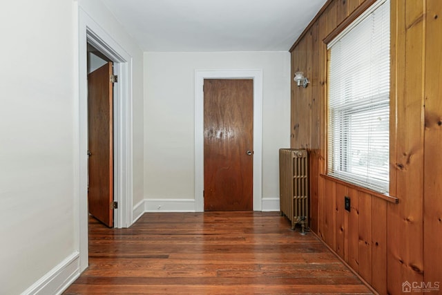 corridor featuring baseboards, radiator, wood finished floors, and wood walls