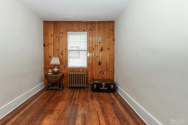 unfurnished room with radiator heating unit, wood finished floors, baseboards, and wood walls