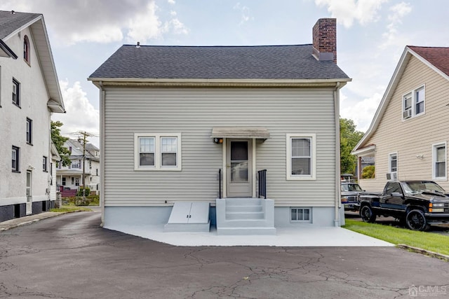 view of front of property featuring entry steps, a shingled roof, and a chimney