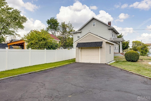 view of side of property featuring fence, a lawn, a chimney, a garage, and driveway