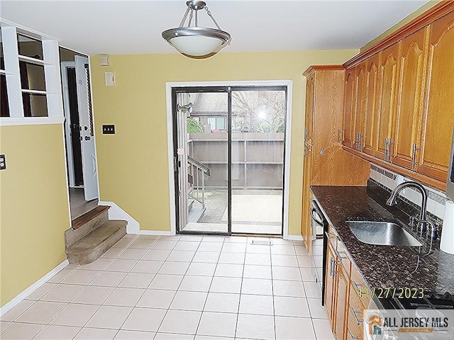 kitchen featuring dishwasher, light tile patterned floors, sink, and dark stone countertops