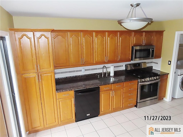 kitchen with dark stone counters, sink, light tile patterned floors, stainless steel appliances, and washer / clothes dryer