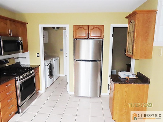 kitchen featuring independent washer and dryer, stainless steel appliances, light tile patterned floors, and dark stone counters