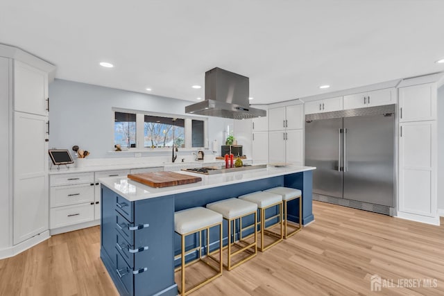 kitchen featuring gas cooktop, built in fridge, island range hood, white cabinetry, and light countertops