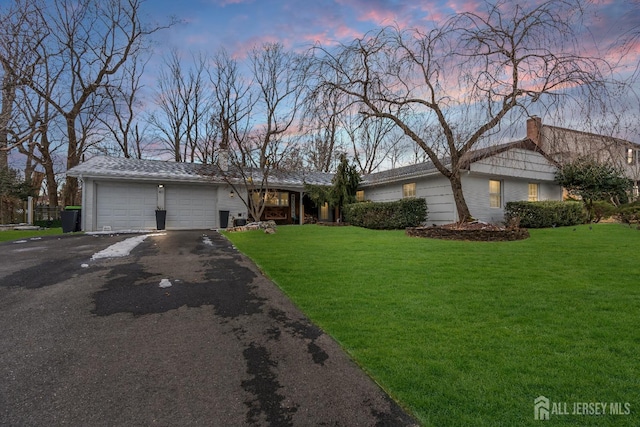 ranch-style home with a garage, driveway, a yard, and a chimney